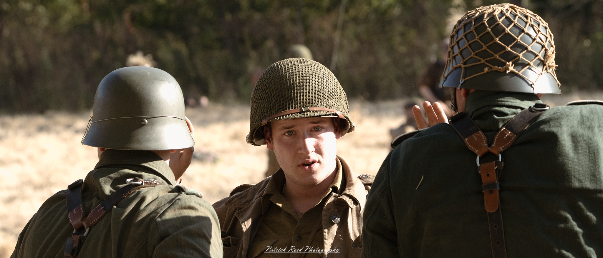 "Scene depicting a World War II prisoner of war (POW) interrogation outdoors, emphasizing the harsh conditions of wartime. A captured soldier in a worn uniform stands against a rough wall, hands bound, with a look of concern and defiance. Surrounding him, military personnel, including an interrogator in uniform, are engaged in questioning, their expressions serious and intense. The backdrop features a rugged landscape, perhaps a battlefield or camp, underscoring the tension and stakes involved in the interrogation process. The image captures the emotional weight of captivity and the struggle for survival."